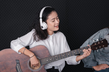 Asian female singer with a passion for music and microphone. While playing her guitar in a professional studio. Music concept, sound recording concept.