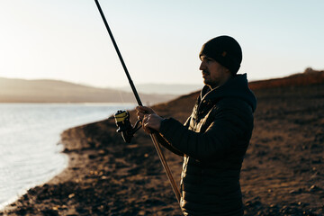 Young fisherman standing on the shore of lake with fishing rod