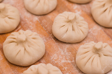Fototapeta na wymiar Three rows of homemade raw khinkali dumplings on a wooden board in flour