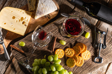 Different types of cheeses, cheese tasting with grapes and crackers and glasses of red wine, top view