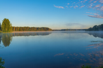 Obraz na płótnie Canvas Morning steam over the Roshchinsky lake, clear sky and mirror-like surface of the water. Holy Trinity Alexander Svirsky Monastery in the Leningrad region, known for architectural monuments.