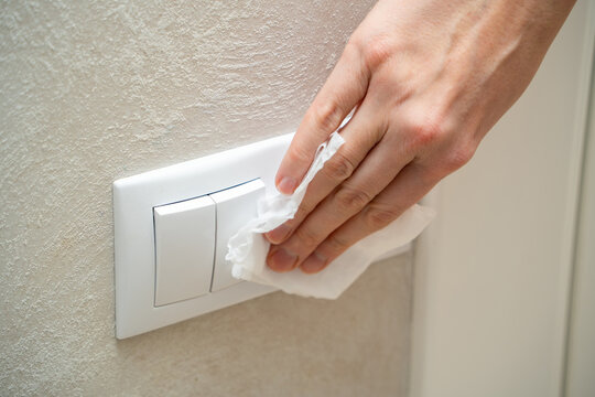 Close-up Of Female Hands Using A Damp Towel To Disinfect A Light Switch. Measures To Prevent The Covid-19 Coronavirus Epidemic