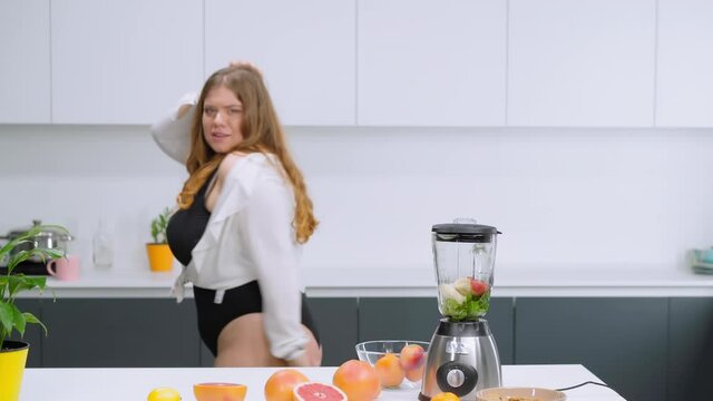 Dancing happy overweight girl dressed in black leotard and white shirt. Dancing in the kitchen curvy body girl blondie preparing fresh fruits juices. Body positive concept. FHD footage. 
