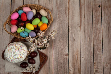 Easter composition. A basket with colorful eggs and a glazed Easter cake decorated with sugar sprinkles on a wooden background.Happy Easter Holidays. Top view. Free space.