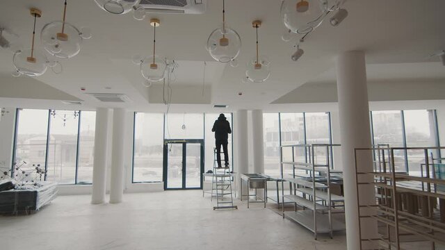 Silhouette of a master of air conditioner repair. The master stands on a ladder in the room without repair and repairs the air conditioner. Room without repair and a specialist working on the ladder.