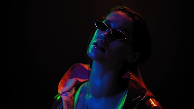 Slow motion in color neon lights beautiful girl wearing sunglasses. Pretty girl with dancing in neon light on black background. Night club, Party. FHD footage. 