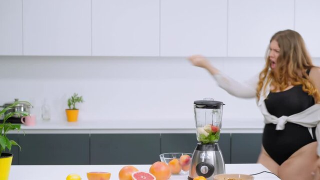 Dieting and nutrition concept. Dancing happy overweight girl dressed in black leotard and white shirt. Dancing in the kitchen curvy body girl blondie preparing fresh fruits juices. FHD footage. 