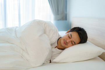 Asian man are sleeping and having good dreams in white blanket in the morning. Rest after work tiring in bedroom at home.