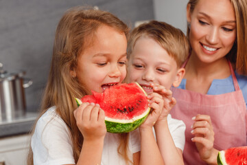 Woman with her daughter and son eating watermelon in kitchen