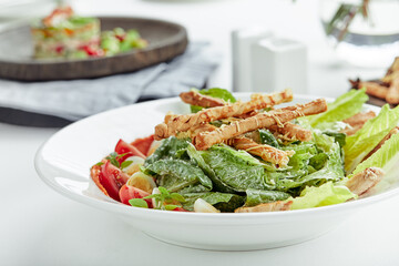 Caesar salad with bread sticks, quail eggs, cherry tomatoes and grilled chicken in plate on white background