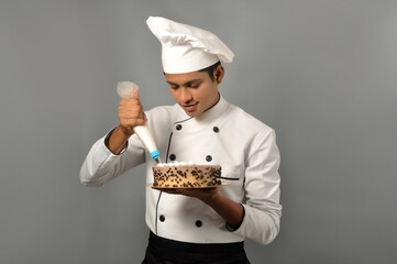 Happy male Indian chef Confectioner decorating chocolate cake, doing icing on the cake