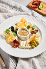 Cheese Food Plate with Olives and Greens. French appetizer cheese board. White restaurant plate on grey table. Wine snacks, gourmet, delicatessen, rustic food concept.