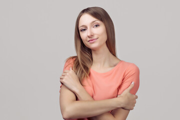 Obraz premium Portrait of gentle lovely beautiful young woman with blonde straight hair hugging herself, expresses self love and care