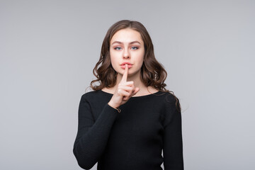 Beautiful serious young woman holding finger at her lips, saying Shh, Hush, demanding keeping...