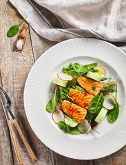 Salmon Salad with Fresh Vegetables. White plate with healthy fish food on wooden table. Healthy, Vegetarian, Restaurant rustic food concept.