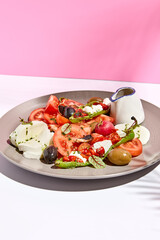 Tomato, olives and mozzarella salad . Restaurant appetizer plate on white table with pink wall. Day sunlight with hard shadow of fern palm leaves. Summer or spring restaurant food concept