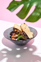 Mussel with bread restaurant plate. Restaurant appetizer plate on white table with pink wall. Day sunlight with hard shadow of monstera palm leaves. Summer or spring restaurant food concept.