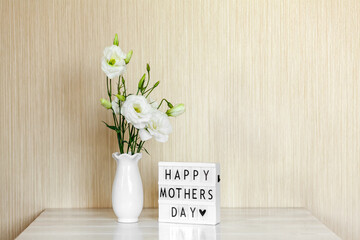 Light box with lettering Happy Mother's Day, white flowers Eustoma or Lisianthus in vase on wooden background with copy space