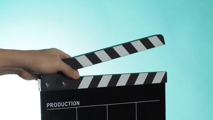 Hand is holding Black clapper board or movie slate on green or Tiffany Blue or or mint background.