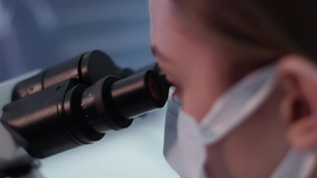 Female doctor working in laboratory. Studying medical samples. Looking through glassware and monitor