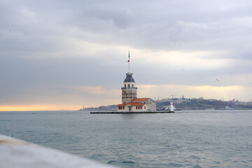 Obraz premium The Maiden's Tower under gray cloudy sky, Bosphorus, Istanbul, Turkey during overcast weather with sunshine reflection in bosporus sea. Groups of seagulls flying on sea. İstanbul Turkey 01.03.2021