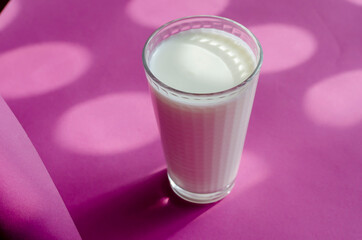 A glass of kefir on a pink surface with shadows.