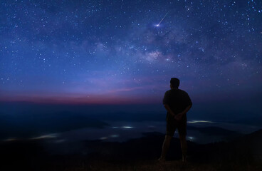 Colorful night sky with stars and silhouette of a standing man on the stone. Blue milky way with...