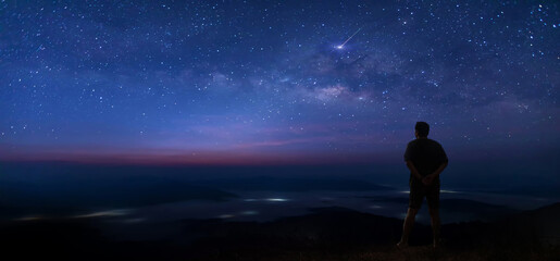 Colorful night sky with stars and silhouette of a standing man on the stone. Blue milky way with...
