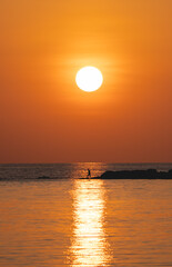 Sunset ocean view. Sun above the sea on orange sky. Fisherman with fishing rod on the rock.
