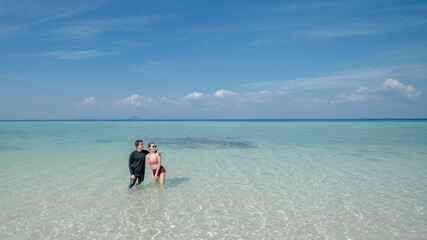 Man holding hand bikini woman walk on sea water by white sand beach. Blue sea and sky landscape. summer vacation.