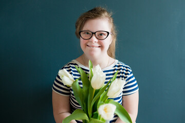 Portrait of teenage girl with Down syndrome standing with flowers on blue background. Disability children. World Down syndrome day.