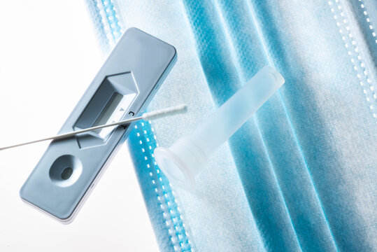 Corona Schnelltest, Testst&auml;bchen, Testkassette und Testr&ouml;rchen liegen auf Gesichtsmaske, Studioaufnahme auf wei&szlig;em Untergrund.