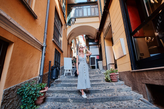 Fototapeta Traveling by Europe. Happy young woman in dress walking by streets in italian old town.