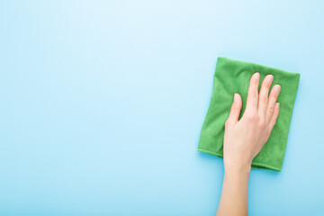 Young adult woman hand holding green rag and wiping table, wall or floor surface in kitchen,...