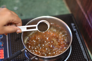 adding black tea leaves and a pinch of herb mixture to boiling water with grated ginger, for...