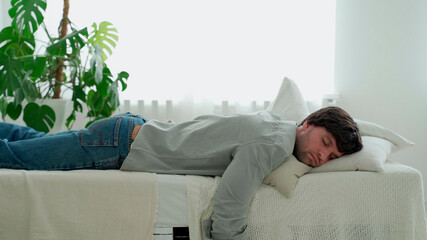 Exhausted young man falling asleep on bed, feeling no energy after hard working day. Businessman...