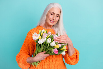 Photo of peaceful joyful elderly lady look touch flowers bouquet isolated on pastel teal color background