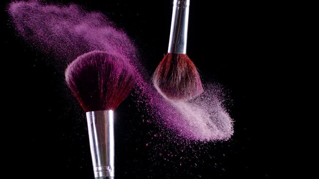 Two makeup brushes collide and cause a swirl of pink powder particles against a black background, slow motion, 300fps. 