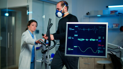 Monitor shows EKG reading of man athlete running on cross trainer and discussing with medical...