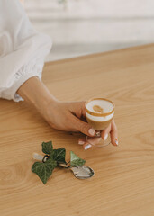Female hand holding a small glass of coffee on a wooden table background.