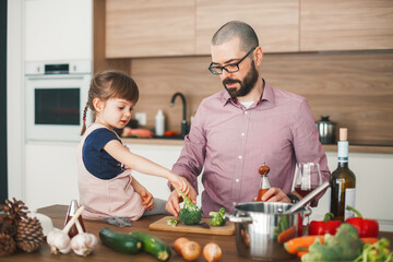 Man and his little daughter are cooking vegetable stew together