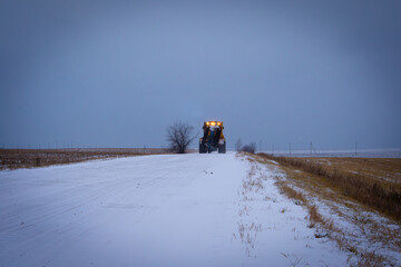 The tractor is driving on a snowy road.