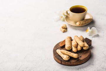 Long shortbread cookies on a dark wooden board with a cup of tea on a light background. Side view with a copy space for the text.