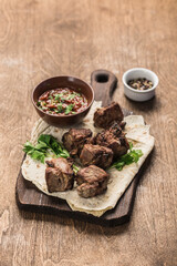 Pork shish kebab on a wooden board with tomato sauce on a dark background. Grilled picnic food. Side view with a copy space for the text.