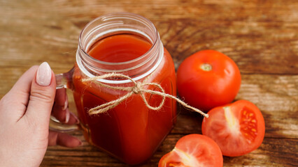 Female hand holds Glass of tomato juice on wooden table. Fresh tomato juice