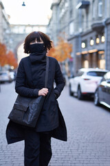 Fashion styled attractive female in total black wear with a black eco bag enjoys a walk along the street. Beautiful girl in fashionable clothes in the European city background