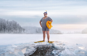 Fuunny overweight, retro swimmer standing by the ice hole in the lake, at the cold sunrise with...
