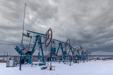 Several Oil pumpjack under gray heavy leaden clouds winter working. Oil rig energy industrial machine for petroleum in the sunset background for design.