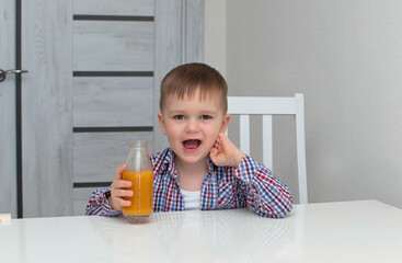 Healthy, cute boy in bright shirt is holding glass and drinking orange juice. Emotionally. Сoncept of healthy lifestyle
