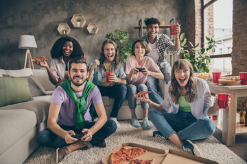 Photo portrait of students in hostel sitting on sofa playing video games with remote controllers eating pizza drinking beer - obrazy, fototapety, plakaty